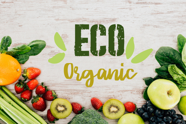 top view of arranged organic strawberries, vegetables and fruits on wooden tabletop with "eco organic" lettering - Foto, afbeelding