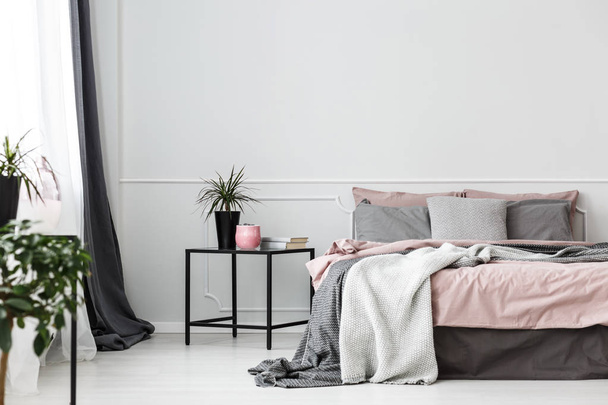 Black, box frame side table next to a cozy bed with gray blankets and pink sheets in an elegant bedroom interior - Foto, Imagen