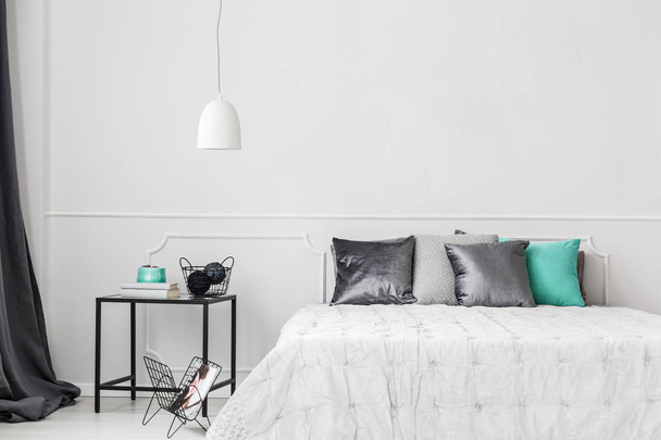 Satin pillows on a minimalist bed by a white empty wall in a trendy bedroom interior with gray and teal green decorations - Fotografie, Obrázek