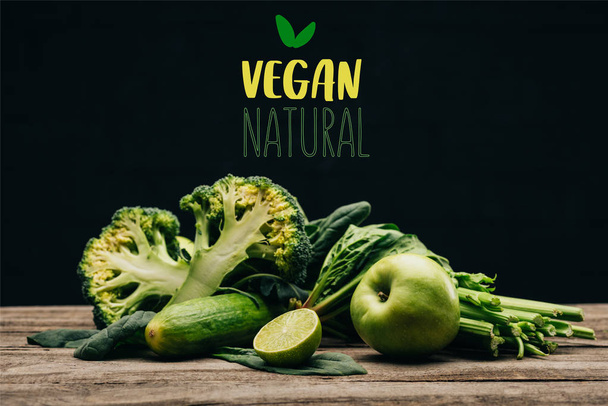 close up view of fresh healthy vegetables and fruits on wooden surface on black with "vegan natural" lettering - Photo, Image