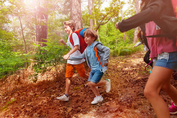Two boys in group of kids run in the forest with backpack in active activity game on summer camp - Foto, afbeelding