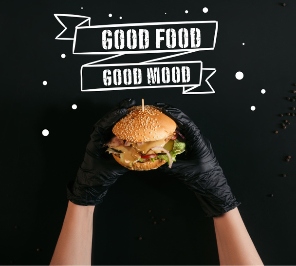 recortado tiro de manos en guantes sosteniendo deliciosa hamburguesa con pavo, verduras y aderezo César en negro con "buena comida - buen humor" inspiración
 - Foto, imagen