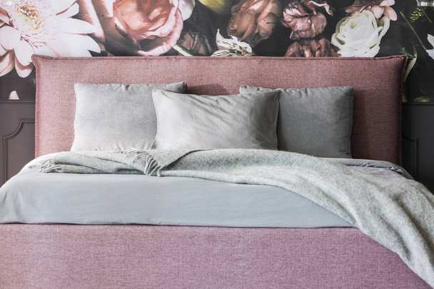 Grey blanket and cushions on pink bed in feminine bedroom interior with flowers wallpaper. Real photo - Foto, imagen