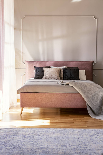 Blanket and pillows on pink bed in simple bedroom interior with carpet and wall with molding. Real photo - Fotoğraf, Görsel