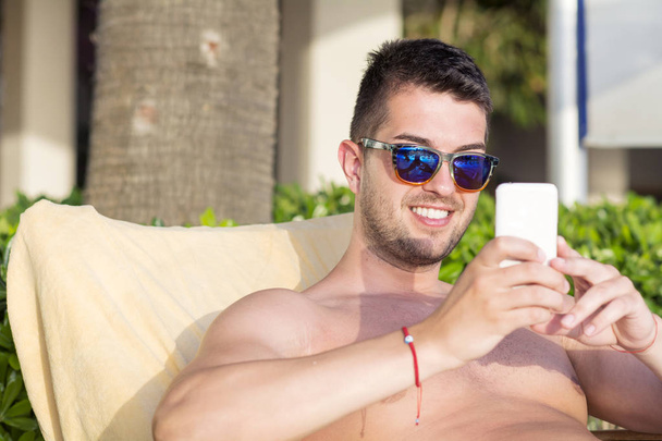 スマートフォンを使ってサングラスをかけた若い男性の休息  - 写真・画像