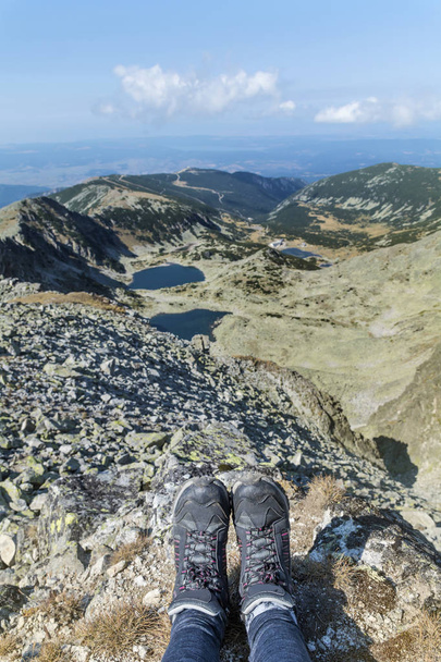 Legs of traveler sitting on a high mountain top with lake view. - Zdjęcie, obraz