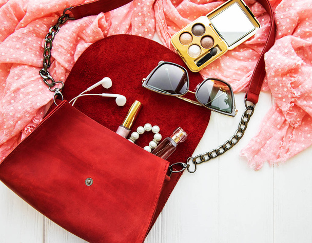 Bolso de cuero rojo con accesorios en una mesa de madera blanca
 - Foto, Imagen