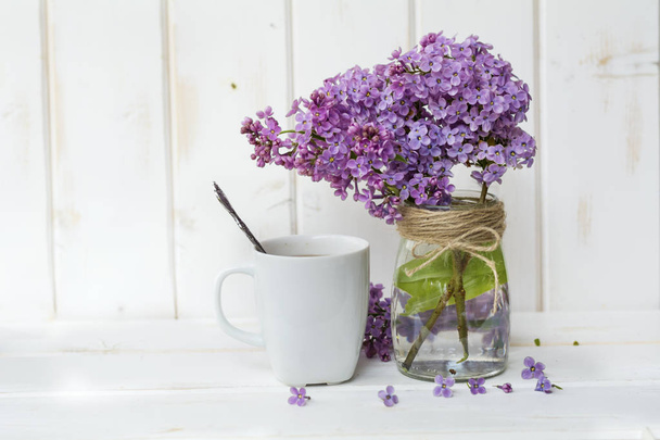 cup of coffee with milk and bouquet of lilac on white  wooden background - Фото, зображення