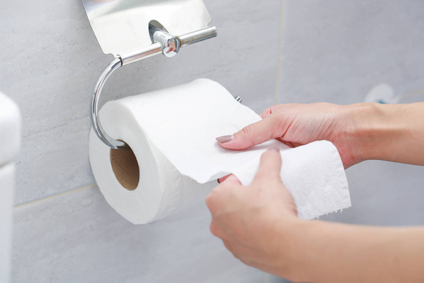 Κοντινό πλάνο του χέρι χρησιμοποιώντας το χαρτί τουαλέτας. - Φωτογραφία, εικόνα