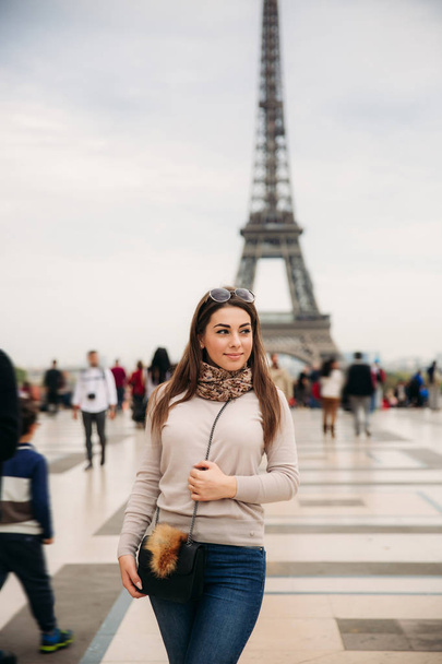 Beautiful girl posing to the photographer against the background of the Eiffel Tower. Autumn photosession. Sunny weather. Beautiful smile and makeup - Photo, Image