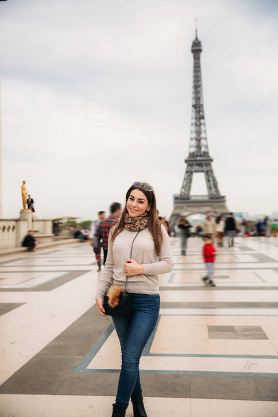 Beautiful girl posing to the photographer against the background of the Eiffel Tower. Autumn photosession. Sunny weather. Beautiful smile and makeup - Fotografie, Obrázek