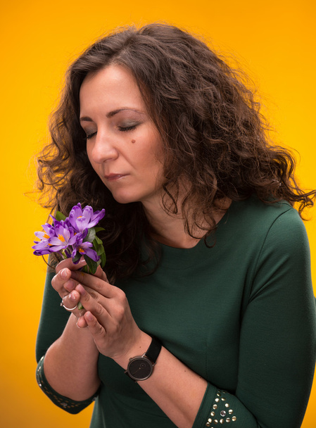 gekrulde vrouw ruikende crocus bloemen met ogen dicht - Foto, afbeelding