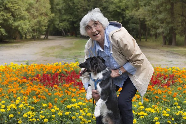 Senior woman hugging her dog in a park with blooming flowers - Photo, Image