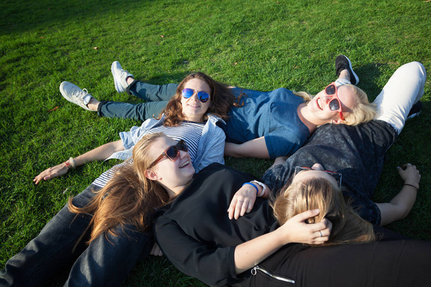 Group of happy smiling carefree young stylish girls  lying on the grass in the park, millenial concept, youth and students, tourism and holidays - Фото, изображение