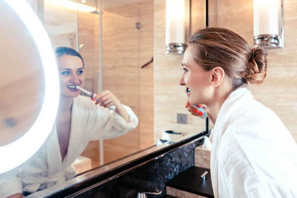 Woman brushing her teeth in luxurious hotel looking at herself - Foto, imagen