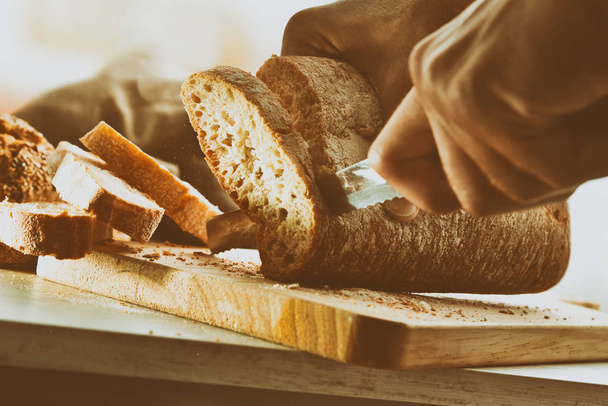 Chef slicing bread in slices on a cutting board in a kitchen bench. Front view. Horizontal composition - Foto, Bild