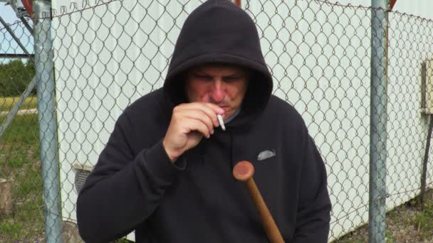 Muž s baseballovou pálkou kouření u plotu - Záběry, video