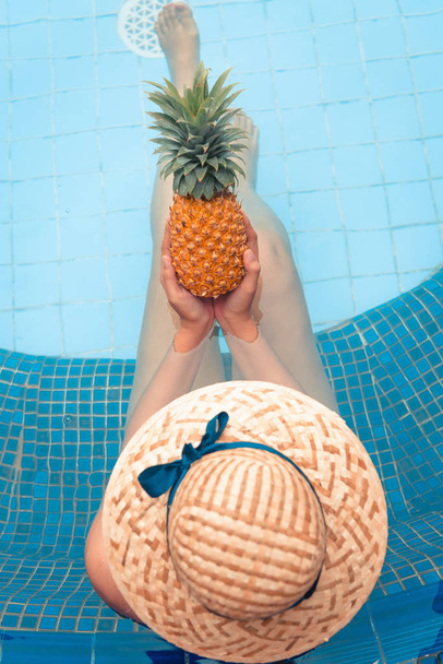Conceito de verão, vista superior da mulher segurando abacaxi e relaxando na piscina
. - Foto, Imagem