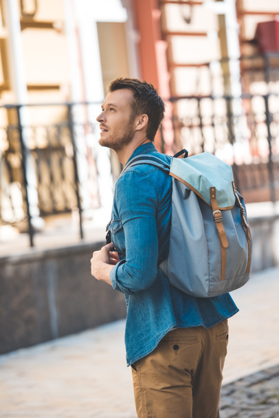 handsome young tourist with backpack walking by street and looking up - 写真・画像