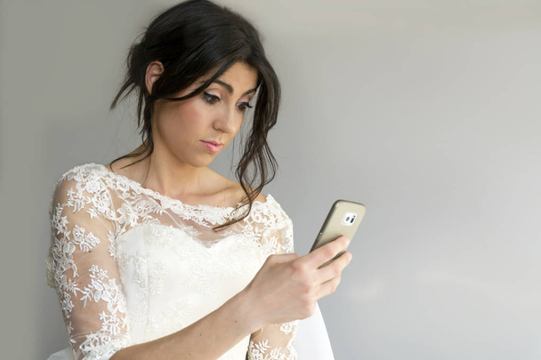 Bride in white dress with brunette hair using smartphone  - Foto, Imagen