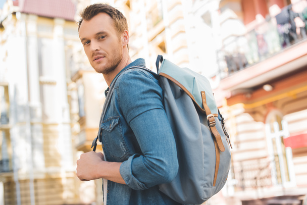 handsome young man with backpack walking by street and looking at camera - Photo, Image