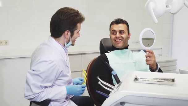 Ammattimainen hammaslääkäri antaa peilin potilaalleen hammashoidon jälkeen
 - Valokuva, kuva