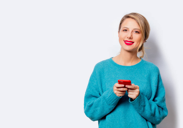 Портрет красивой белой улыбающейся женщины в голубом свитере с мобильным телефоном на белом фоне, изолированный
. - Фото, изображение