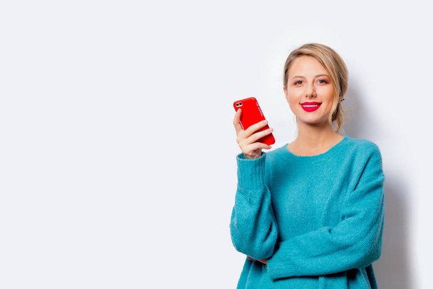 白い背景の分離上の携帯電話に青いセーターの美しい白い笑顔の女性の肖像画. - 写真・画像