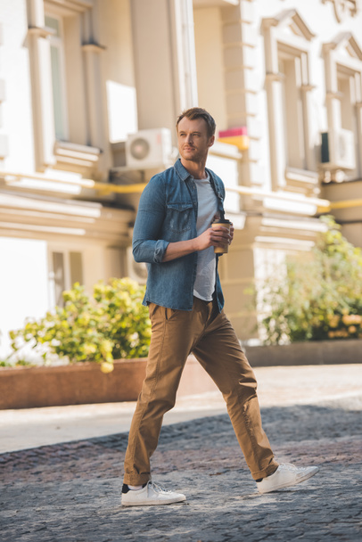 attractive young man with coffee to go walking by city - Foto, Imagen