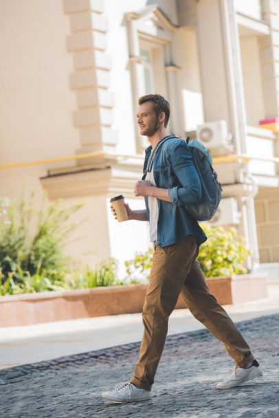 attractive young man with coffee to go and backpack walking by city - Photo, Image