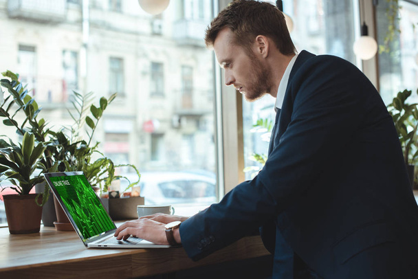 vista laterale di uomo d'affari concentrato che lavora su laptop con lettering commerciale online sullo schermo a tavola con tazza di caffè nel ristorante
 - Foto, immagini
