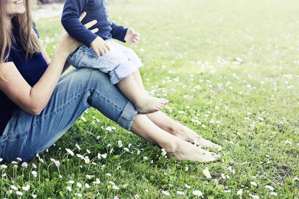 Low section of woman relaxing on green grass with baby boy - 写真・画像
