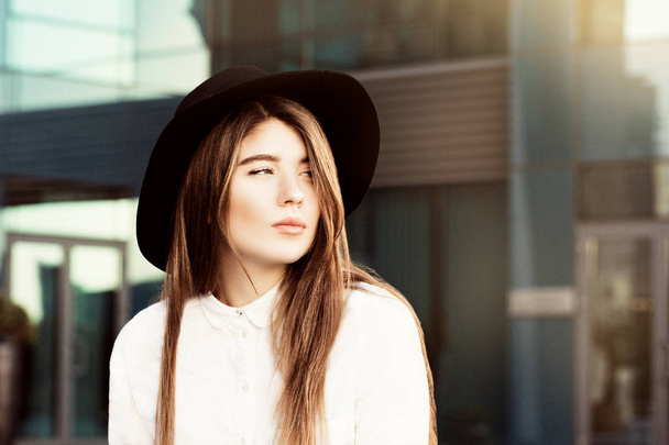 Retrato al aire libre de una adolescente reflexiva con sombrero negro y camisa blanca
 - Foto, Imagen