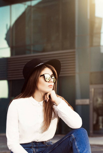Egy csinos lány a divatos napszemüveg, fekete kalapot és fehér inget viselő szabadtéri portréja - Fotó, kép