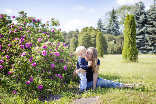 Young woman relaxing on green meadow with little son in sunny park - Fotografie, Obrázek