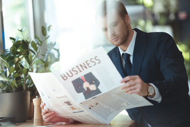 focused businessman in suit reading newspaper in cafe - Photo, Image