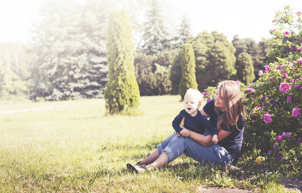 Young woman relaxing on green meadow with little son in sunny park - Fotó, kép