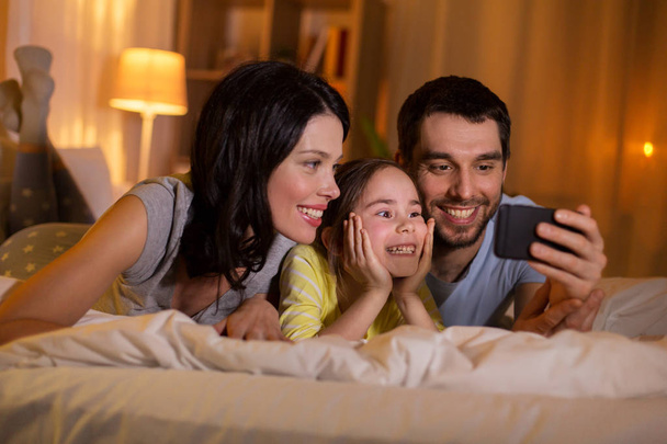 happy family with smartphone in bed at night - Φωτογραφία, εικόνα