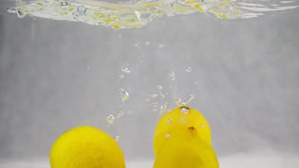 Três limões amarelos caem simultaneamente na água com bolhas. Vídeo em câmera lenta
. - Filmagem, Vídeo