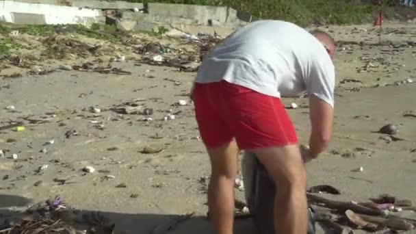 Mann putzt im Urlaub den Strand - Filmmaterial, Video