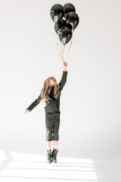 dreamy child jumping or flying with black balloons on grey - Foto, afbeelding