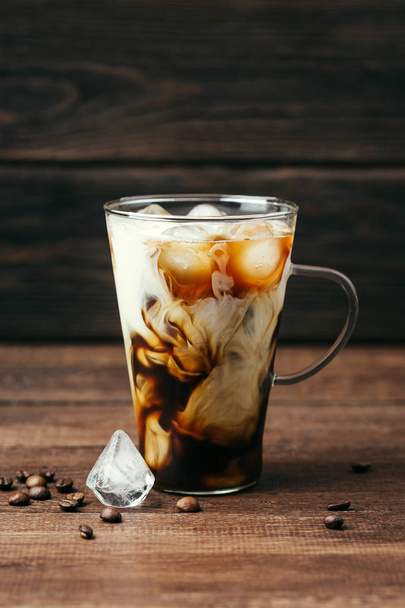 Černá káva se smetanou v transparentní hrnek na dřevěné pozadí - Fotografie, Obrázek