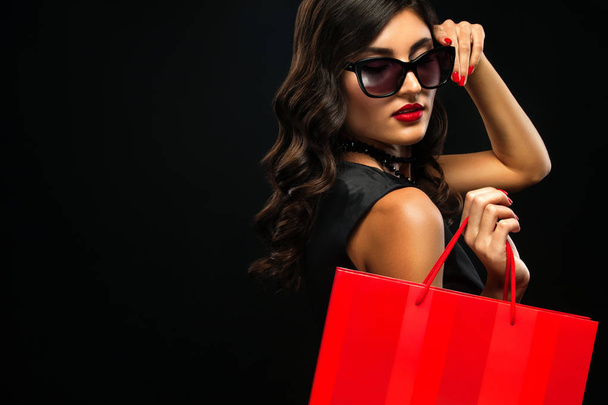 Black friday sale concept. Shopping woman holding red bag isolated on dark background in holiday - Foto, Imagem