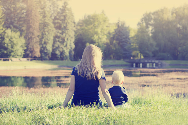 Mother relaxing on green grass with toddler son in sunny park - Фото, изображение