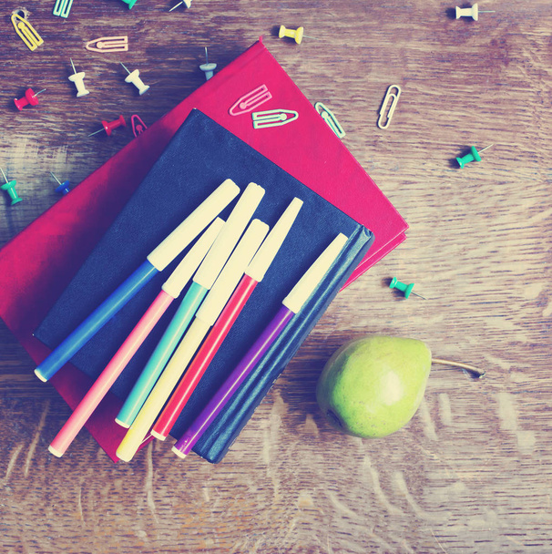 Groene peer, boeken stack en vilt pennen op hout - Foto, afbeelding