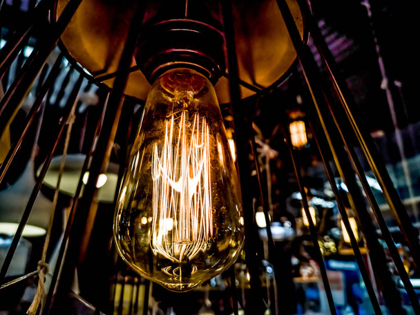 Tungsten orange light bulb hanging on the inside of the building with a black iron fence around,Lighting in buildings with multi-colored electric lamps,soft focus.high contrast format. - Photo, Image