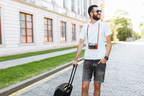Young hipster male hiker with beard, walks around town with a suitcase and a camera around my neck - Fotoğraf, Görsel