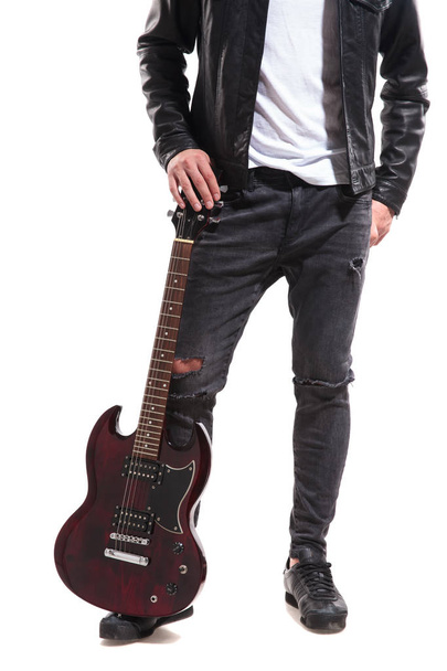 pernas de roqueiro vestindo jeans rasgado e jaqueta de couro segurando sua guitarra no chão
 - Foto, Imagem