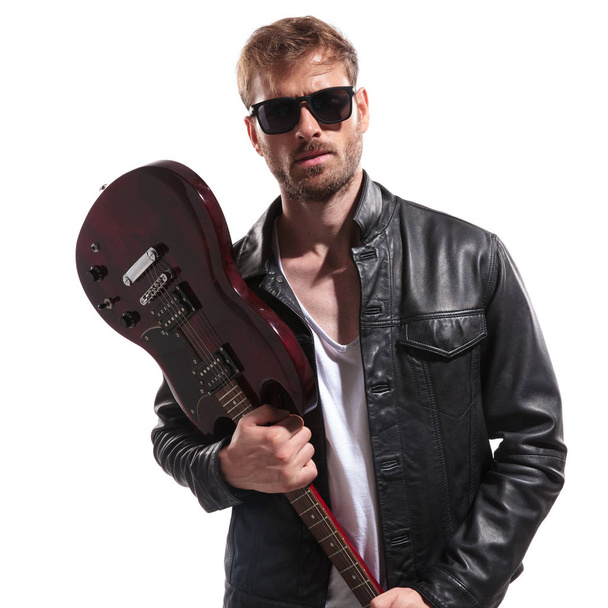 portré fiatal rock star rajta napszemüveg és a bőrdzseki akarnak törni az elektromos gitár, állva, fehér háttér - Fotó, kép