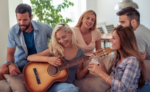 Happy friends playing guitar and listening to music at home. - Photo, Image